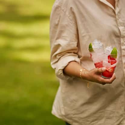 Absolut Juice Strawberry and Soda in two tall glasses with crushed ice and sliced strawberries, labeled bottle in hand