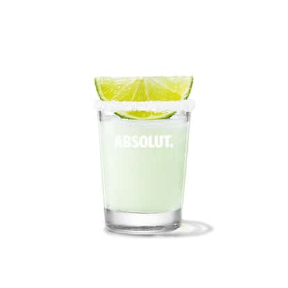 Pale green lime cocktail in an Absolut rocks glass with a salted rim and lime wedge on white background.