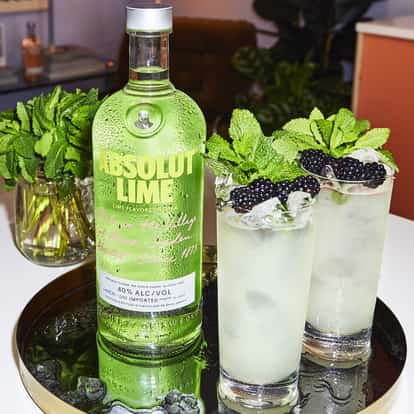 Absolut Lime Lemonade in two tall glasses with mint and blackberry garnishes on a tray beside its bottle