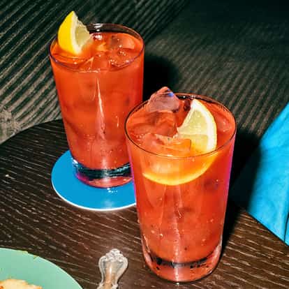 Absolut Long Bloody Mary served in two highball glasses with ice and lemon wedges on a wood table