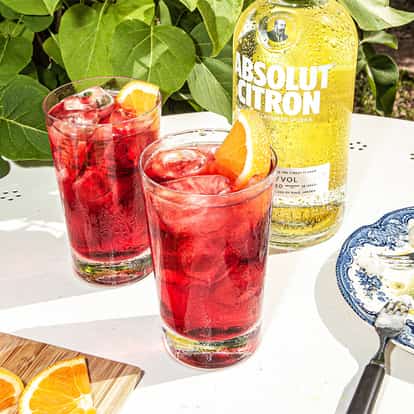 Absolut Long Cosmopolitan in a highball glass with ice and an orange wedge beside a vodka bottle