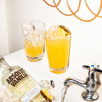Absolut Long Passionstar served in a tall glass with pineapple wedge, Absolut Vanilia bottle on ice in sink
