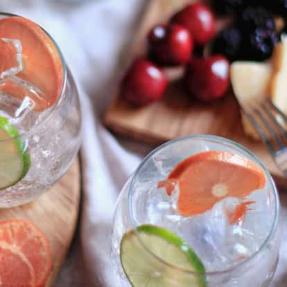 Absolut Mandrin Soda in two stemless glasses with ice, lime and mandarin slices on wooden board