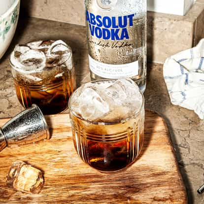 Mind Eraser in two short rocks glasses with ice on a wooden board and an Absolut vodka bottle behind