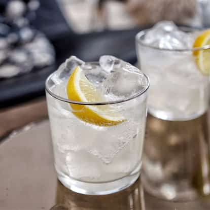 Absolut Vodka in a rocks glass with ice and a lemon wedge on a mirrored surface