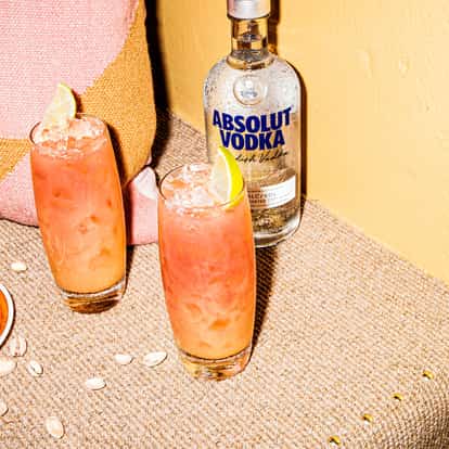 Absolut vodka bottle beside two highball glasses of pink cocktails garnished with lime
