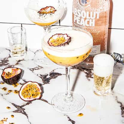 Absolut Peach Passion Star Martini in a coupe glass with halved passion fruit and a labeled bottle behind