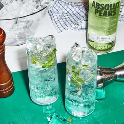 Absolut Pears Highball served in two glasses with ice and thyme sprigs beside a bottle and jigger