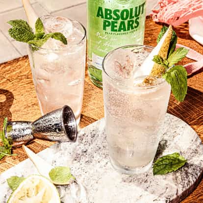 Absolut Pears Sizzle served in a highball glass with ice, pear wedge and mint sprig on a wooden table