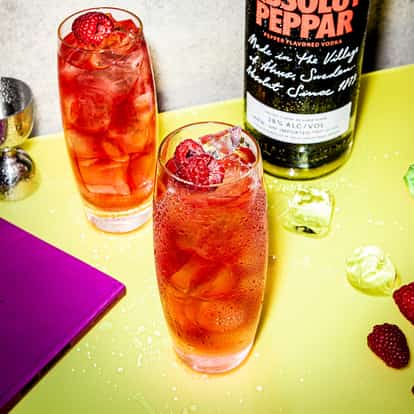 Absolut Peppar Alert in two highball glasses with ice and raspberries on a table