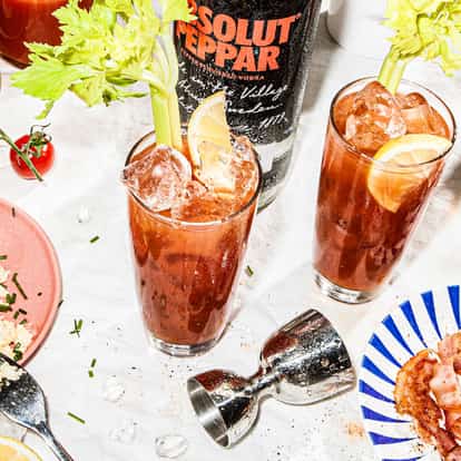 Absolut Peppar Bloody Mary in two tall glasses with ice, celery stalks and lemon wedges on white tablecloth