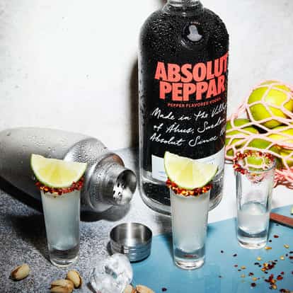 Absolut Peppar Drop in three shot glasses with chili-rimmed lime wedges and a vodka bottle in the background