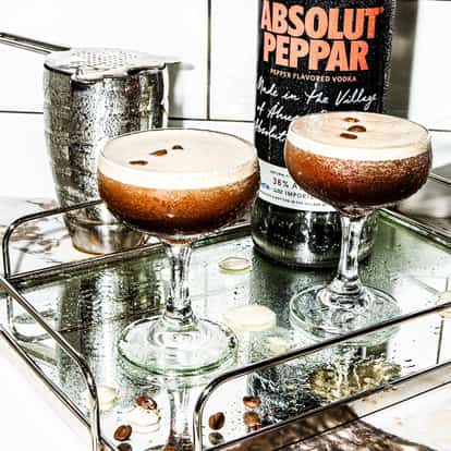 Absolut Peppar Espresso Martini in coupe glasses on a tray with three coffee beans each and a bottle behind