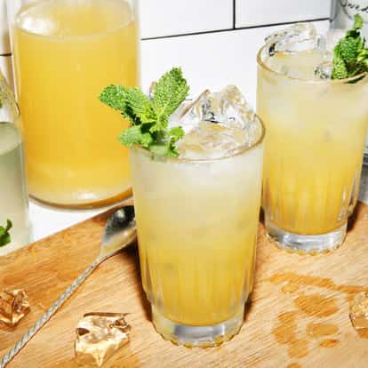 Absolut Pineapple Sting in a highball glass with ice and a mint sprig on a wooden board