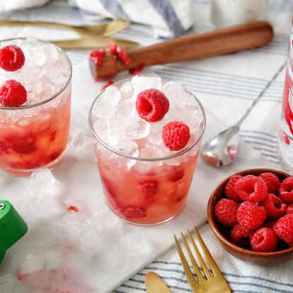 Two Raspberri Blimey cocktails garnished with two raspberries next to a bottle of Absolut Raspberri.