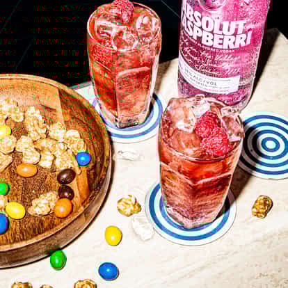 Absolut Raspberri with Cranberry Juice served in a highball glass with ice and raspberries on a stone tabletop