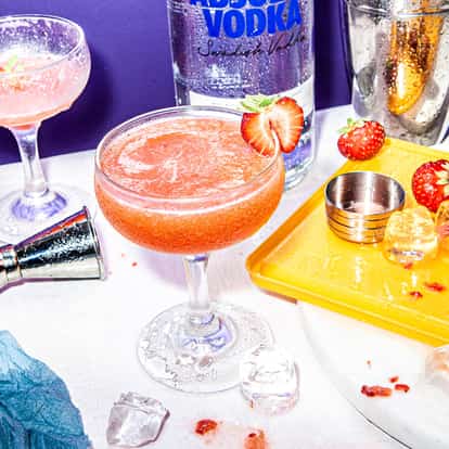 Absolut Strawberry Martini in a coupe glass with a strawberry on the rim and a vodka bottle in the background