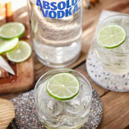 Absolut Vodka Gimlet in a rocks glass with ice and a lime wheel on a wooden table with a vodka bottle behind