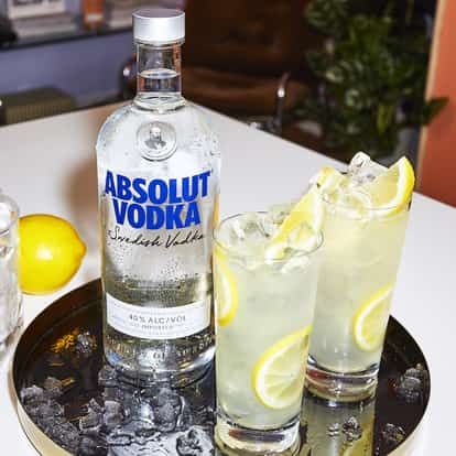 Absolut Vodka Lemonade served in two tall glasses garnished with lemon slices on a round black tray.