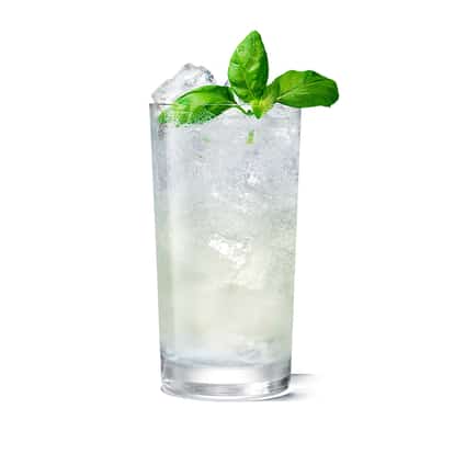 Collins glass filled with a pale cocktail, crushed ice and basil garnish on white background.
