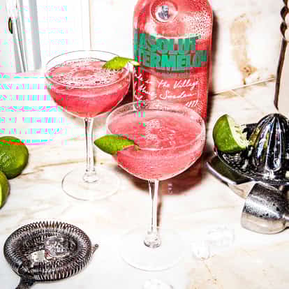 Cosmopolitan cocktails made with Absolut Watermelon next to a bottle of Absolut Watermelon.