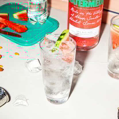 Absolut Watermelon Fizzy in a highball glass with ice and a watermelon wedge, bottle labeled Watermelon visible