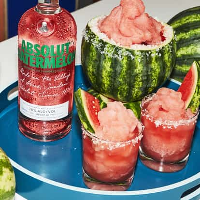 Absolut Watermelon frozen vodkarita next to a bottle of Absolut Watermelon and fresh watermelon.
