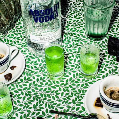 After Eight three shot glasses and two espresso cups on a patterned tablecloth beside an Absolut Vodka bottle