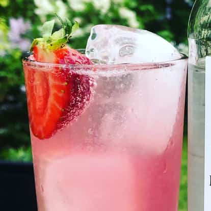 Ahus Revisited in a highball glass with large ice and a halved strawberry beside a bottle with a visible label