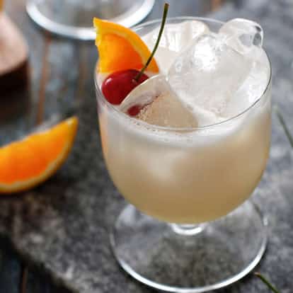 A short glass filled with a golden-brown Amaretto Sour cocktail, topped with frothy foam, garnished with a cherry and orange slice.