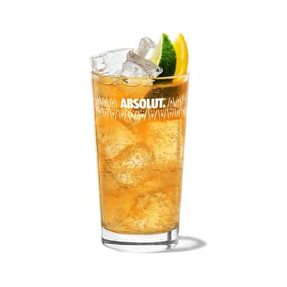 Anejo Highball in an Absolut highball glass garnished with lime and orange wedges on white background.