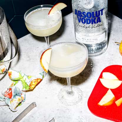 Apple Martini served in a chilled coupe glass with apple slice garnish and an Absolut Vodka bottle on a marble surface