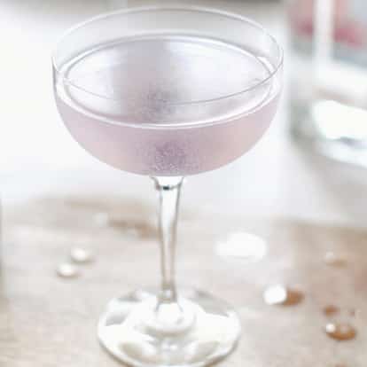 Aviation in a chilled coupe glass on a wooden board beside a second coupe