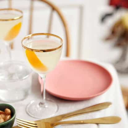 Balalaika in a coupe glass with orange peel twist and Absolut Vodka bottle in background on white surface