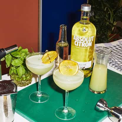 Basil Lemon Drop Martini in two coupe glasses with grilled lemon wheels and an Absolut Citron bottle on a cutting board