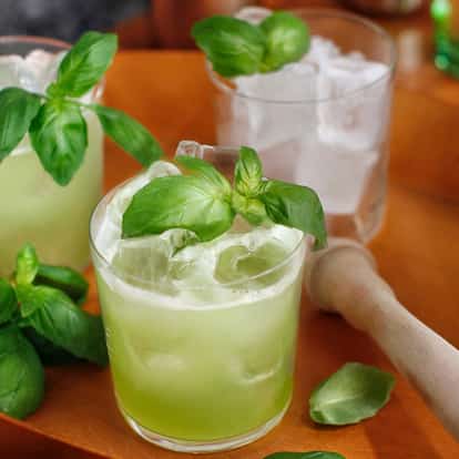 Basil Smash served in rocks glasses with ice and basil leaves on a wooden tray with a muddler