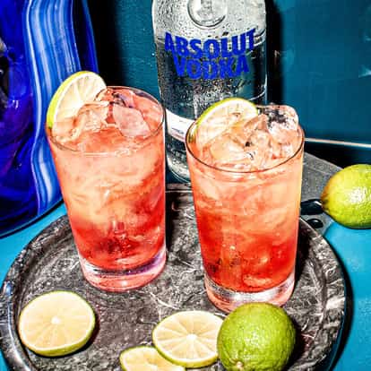 Bay of Passion in two highball glasses with ice and lime wheels and an Absolut Vodka bottle behind on tiled surface