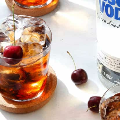 Black Russian in a rocks glass with ice and cherry next to an Absolut Vodka bottle on white background
