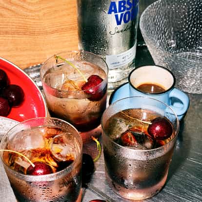 Black Russian served in three rocks glasses with ice and cherries and an Absolut vodka bottle on metal surface