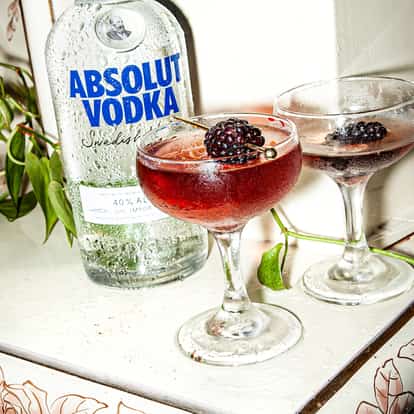Blackberry Martini in two coupe glasses with blackberries on picks beside an Absolut Vodka bottle