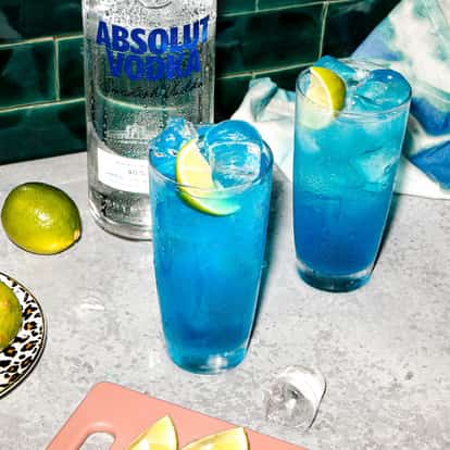 Two Blue Andy cocktails on a table next to a bottle of Absolut Vodka.
