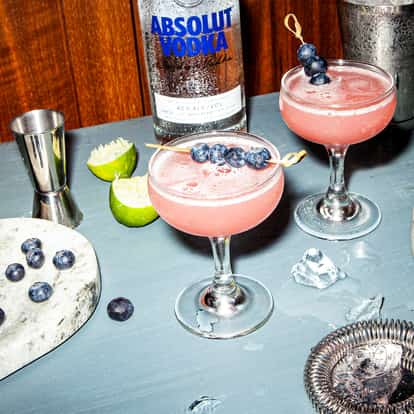 Blue Raspberry Martini in a coupe glass with a blueberry skewer and an Absolut Vodka bottle in the background