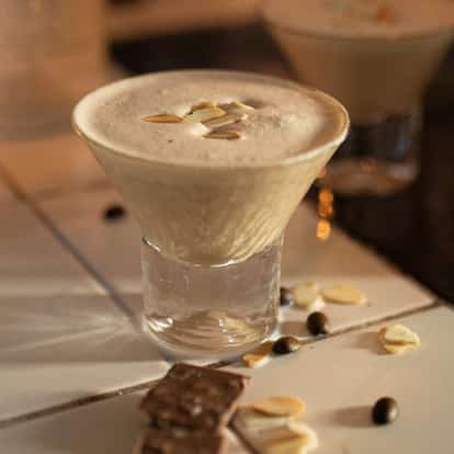 Burnt Toasted Almond in a stemmed glass with foam and almond slices on tiled surface