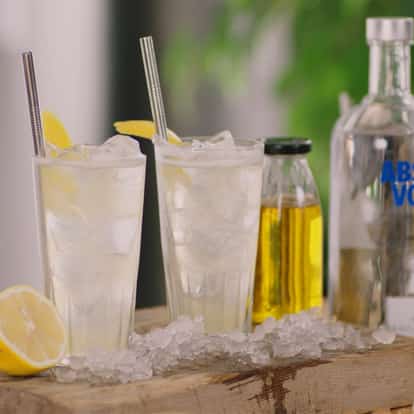 Business Time two iced tall glasses with lemon wedges and straws on board with Absolut Vodka bottle at right