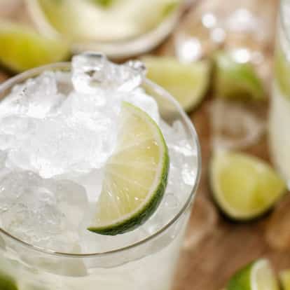 Caipirinha in a rocks glass with crushed ice and a lime wedge on a wooden surface