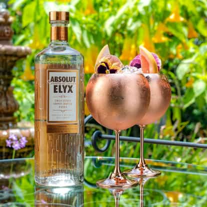 Casino Royale in two goblets garnished with pansies and grapefruit beside Absolut Elyx bottle on glass table