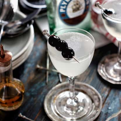 Casino in a coupe glass with a skewer of three cherries on a wooden table