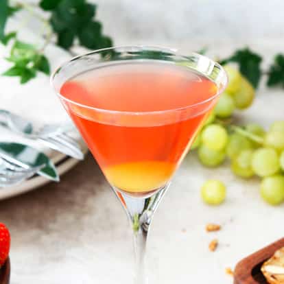 Charlie served in a stemmed martini glass with a layered base and cluster of grapes and strawberries on table