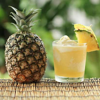 Chi-chi frozen in a rocks glass with a pineapple wedge and whole pineapple on a bamboo mat
