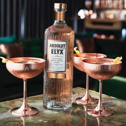 Copper Bullet with an Absolut Elyx bottle and three coupes with lemon twists on a stone table